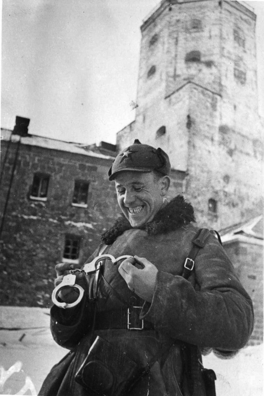Советский офицер рассматривает финские наручники, найденные в Выборгском замке. На заднем плане видна башня Олафа.